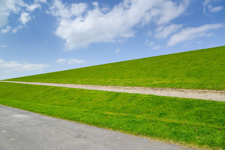 Green grassy dike with path under blue sky