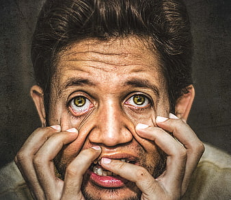 Close-up portrait of a terrified man with wide eyes and hands on face