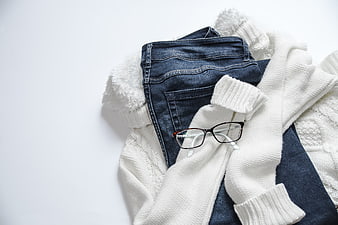 Flat lay of blue jeans, white sweater, and glasses on white background