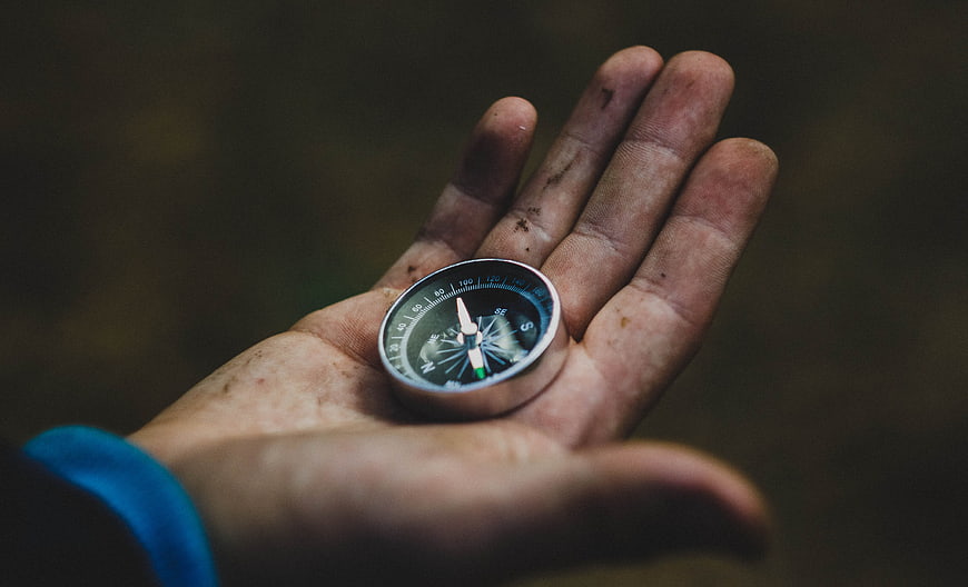 Dirty hand holding compass in forest