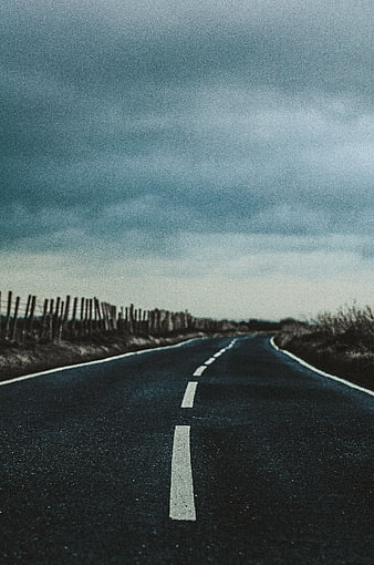 Empty asphalt road stretching into distance under cloudy sky