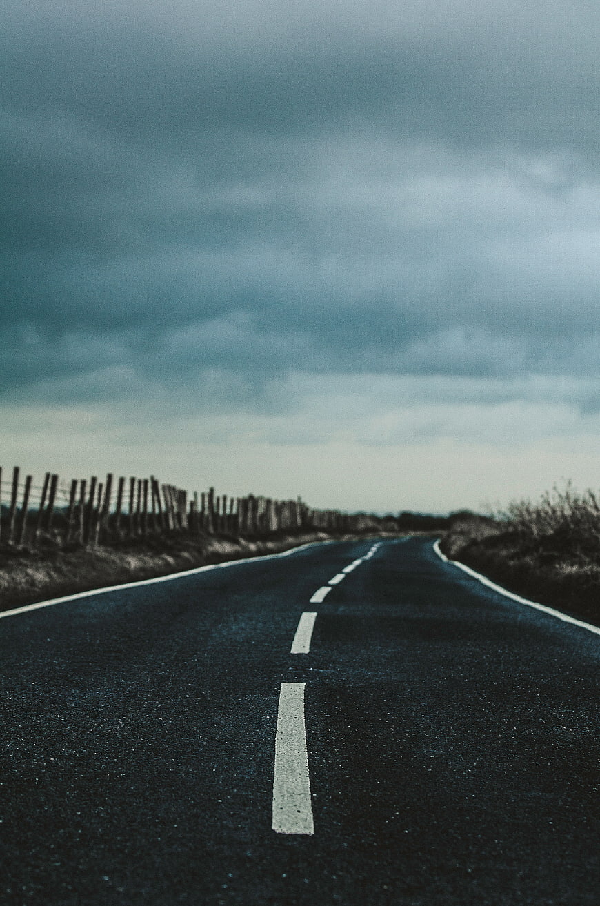 Empty asphalt road stretching into distance under cloudy sky