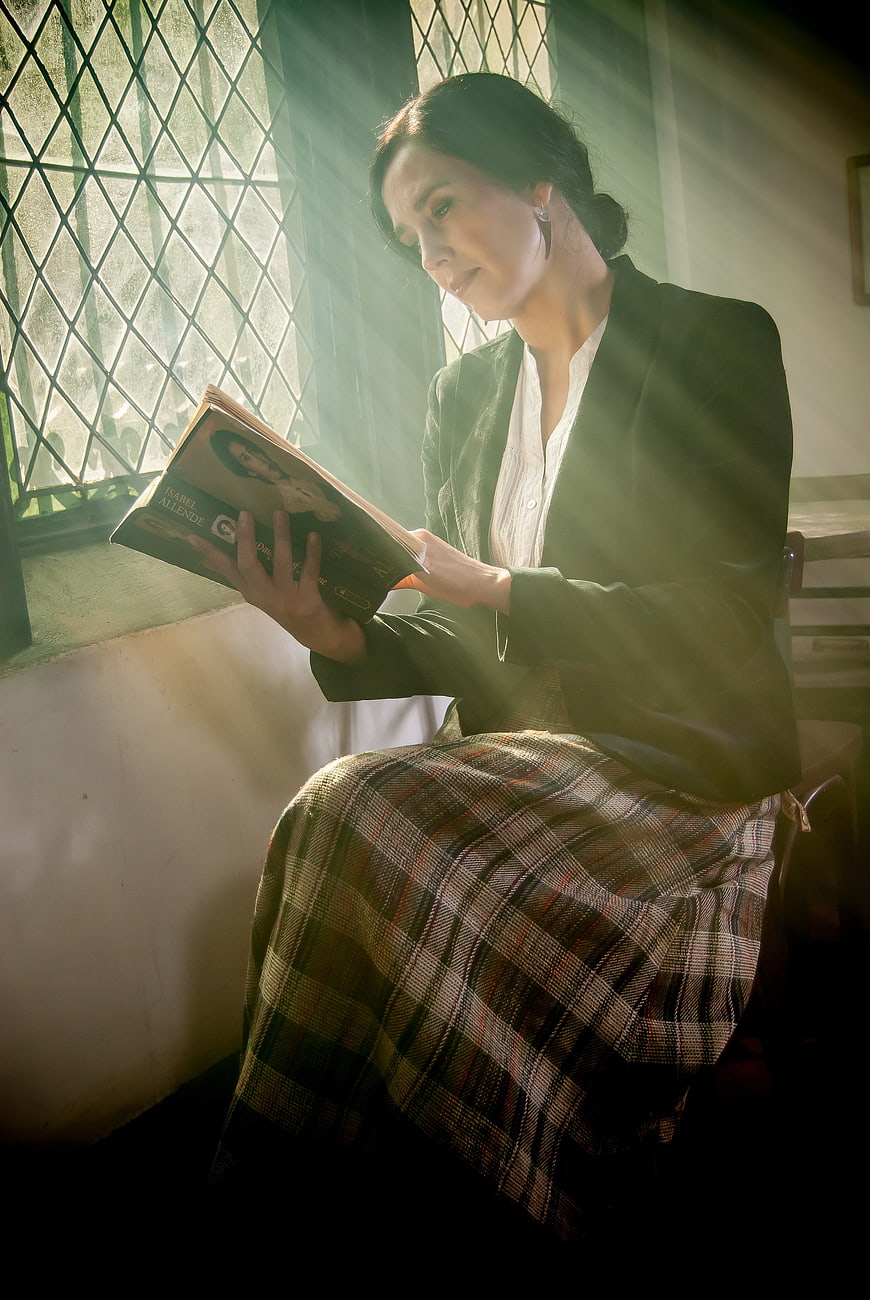 Woman reading book by window with dramatic light rays