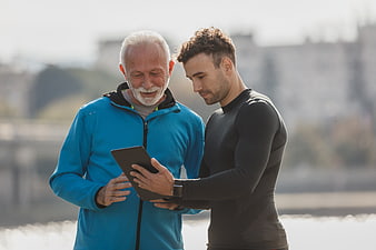 Senior man and young trainer reviewing tablet outdoors