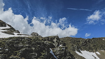 Lone Hiker Standing on Rocky Mountain Peak Under Blue Sky