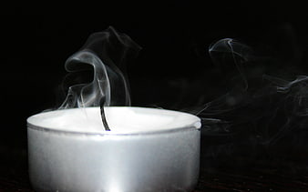 Blown out tea light candle with smoke on black background