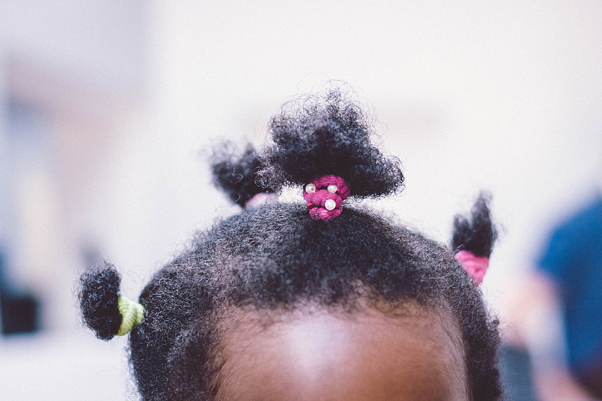 Close-up of child's natural hair styled in puffs with colorful bands