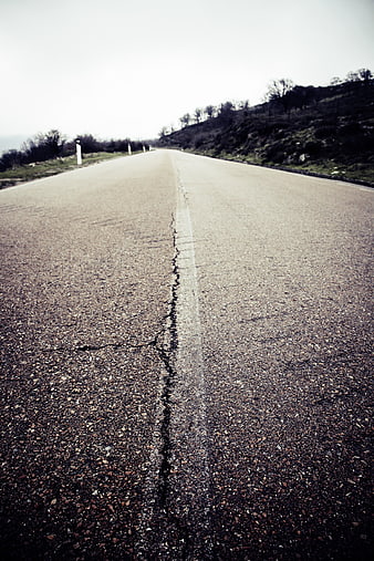 Low angle view of cracked asphalt road stretching into distance