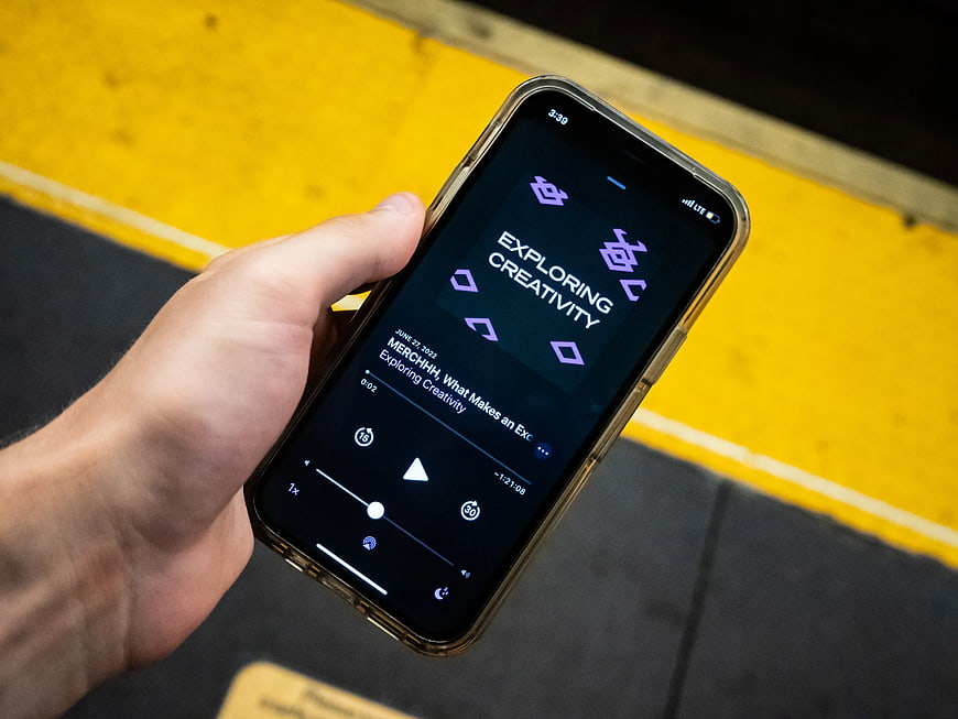 Hand holding smartphone playing podcast on subway platform