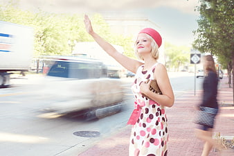 Young woman in vintage polka dot dress hailing a car on city street