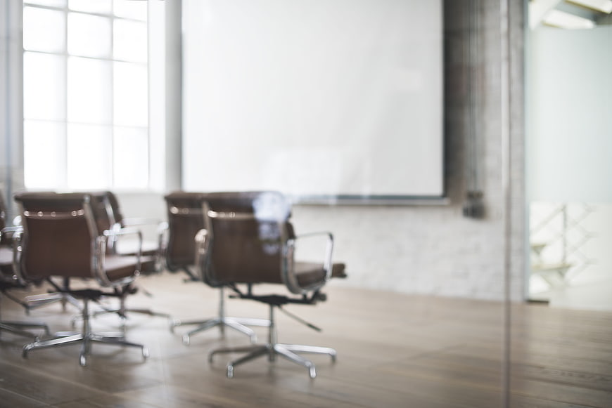 Blurred modern office conference room with brown leather chairs and whiteboard