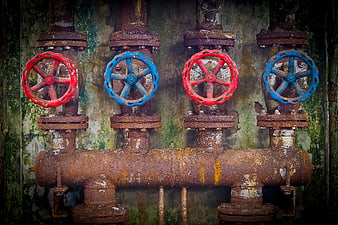 Rusty Industrial Valves with Red and Blue Handwheels on Weathered Wall