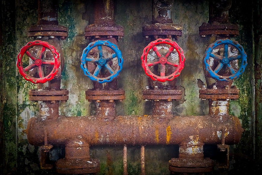 Rusty Industrial Valves with Red and Blue Handwheels on Weathered Wall