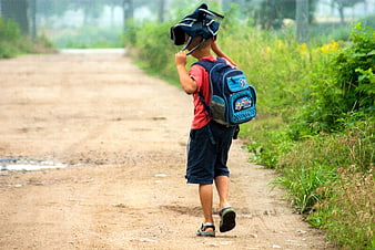 Young boy walking on rural dirt road with school backpack