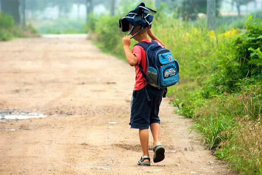 Young boy walking on rural dirt road with school backpack
