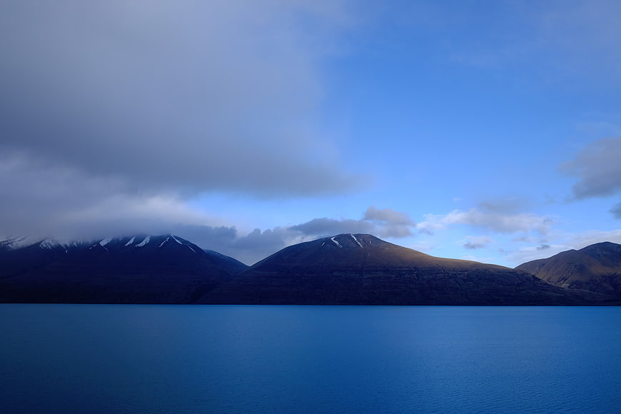 Serene Blue Lake with Snow-Capped Mountains and Cloudy Sky