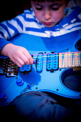 Young boy playing a blue electric guitar with colorful strings