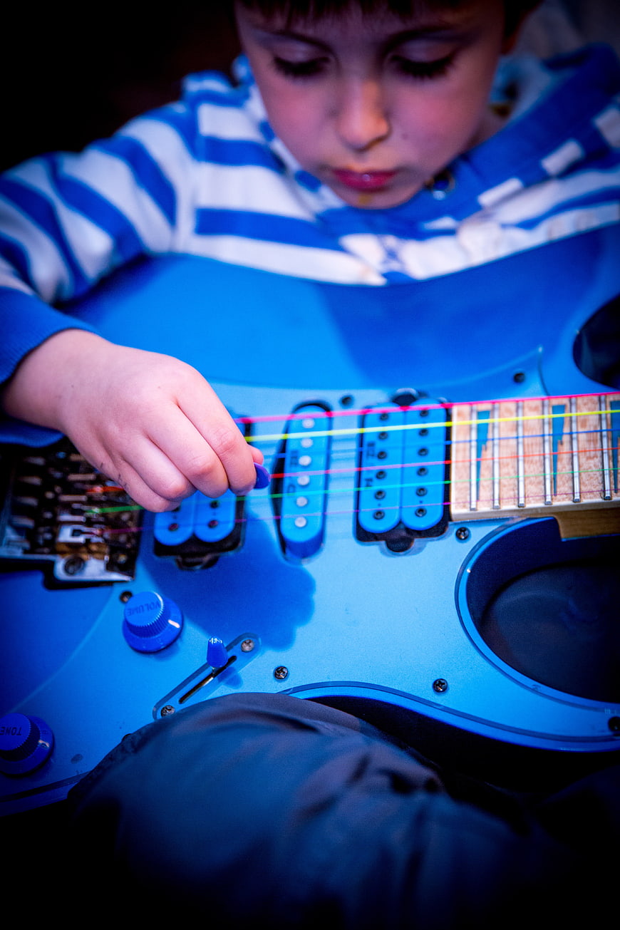 Young boy playing a blue electric guitar with colorful strings
