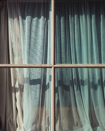 Sunlit sheer curtains behind a rustic wooden window frame