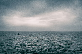 Lone Sailboat on Moody Overcast Ocean Horizon