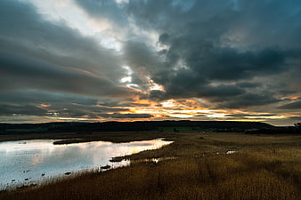 Dramatic sunset over marshland with golden light breaking through clouds