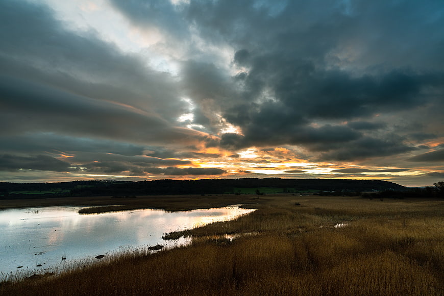 Dramatic sunset over marshland with golden light breaking through clouds