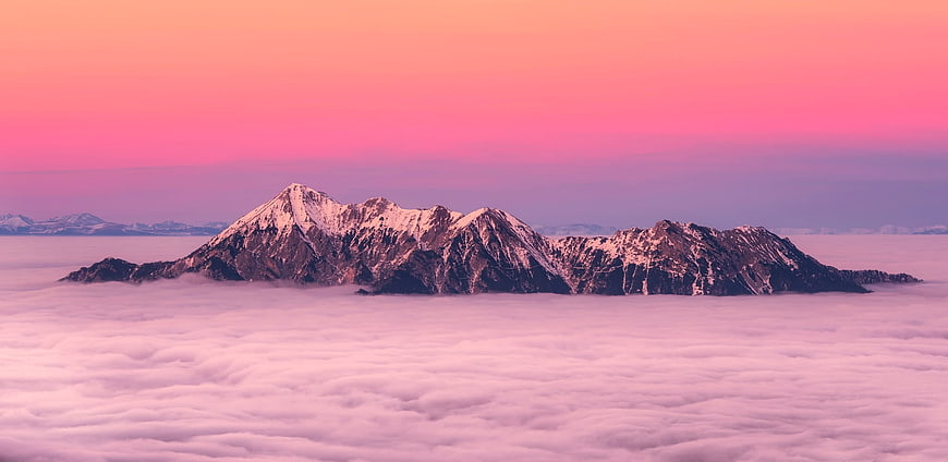 Snowy mountain range rising above a sea of clouds at pink sunrise