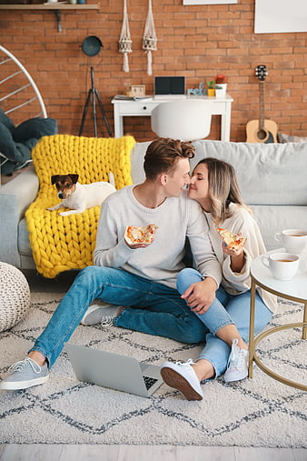Happy couple eating pizza on living room floor with dog