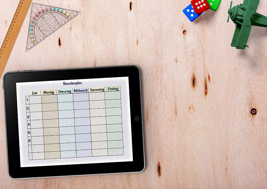 Digital weekly timetable on tablet with school supplies on wooden desk