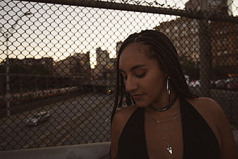 Portrait of young woman with braids against urban fence at dusk