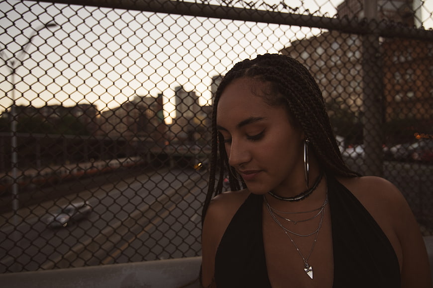 Portrait of young woman with braids against urban fence at dusk