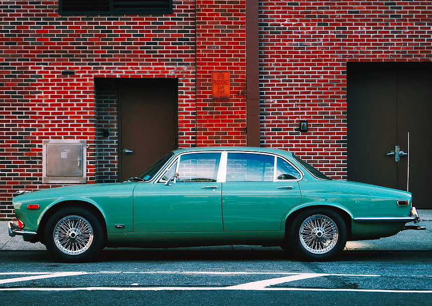 Vintage Green Classic Car Parked Against Red Brick Wall