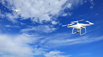 Two White Drones Flying in Blue Sky with Clouds