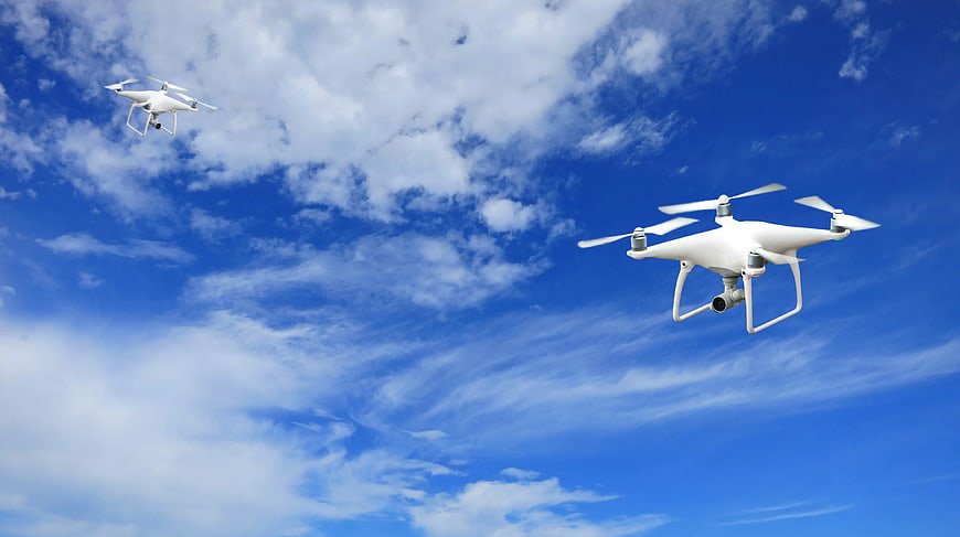 Two White Drones Flying in Blue Sky with Clouds