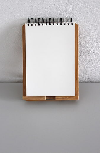 Blank spiral notebook on wooden stand against white wall