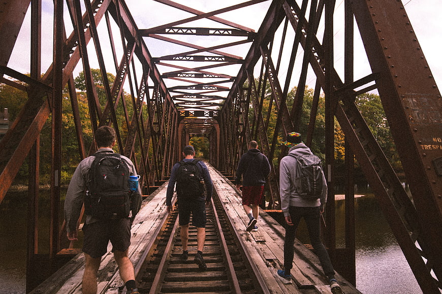 Group of Hikers Walking on Rusty Railroad Bridge