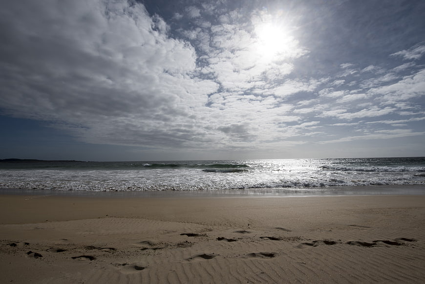 Footprints on sandy beach with ocean waves and cloudy sky