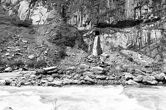 Black and white waterfall cascading from cliff into rocky river rapids