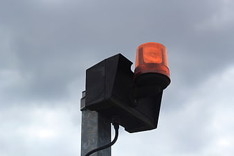Orange emergency warning light on a metal pole against a cloudy sky