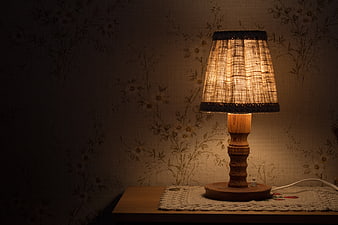 Warm rustic wooden table lamp glowing against vintage floral wallpaper