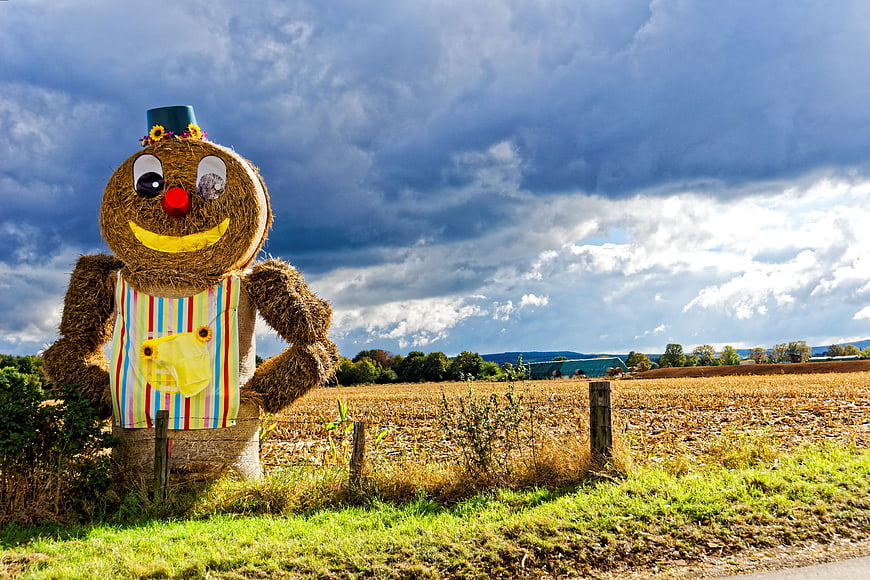 Colorful Hay Scarecrow in Harvested Field Under Dramatic Sky