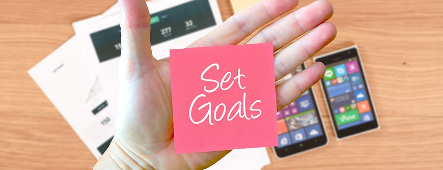 Hand holding pink sticky note with Set Goals text
