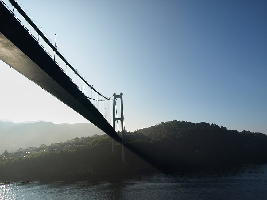 Suspension Bridge Silhouette Over Misty Water and Hills