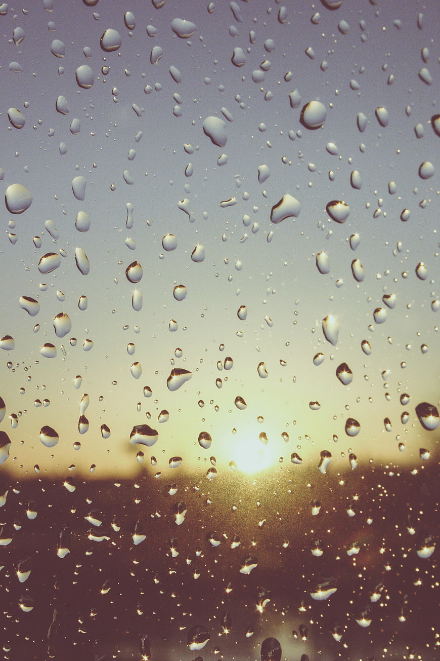 Raindrops on Window Glass with Blurred Sunset Background