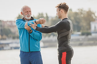Senior man stretching with personal trainer outdoors