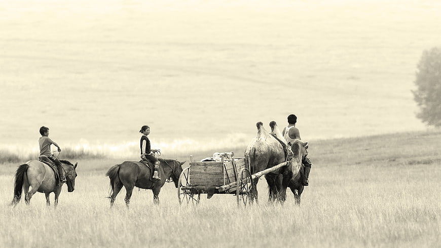 Mongolian family on horseback and camel cart in steppe landscape