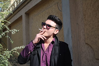 Young man in sunglasses smoking cigarette outdoors