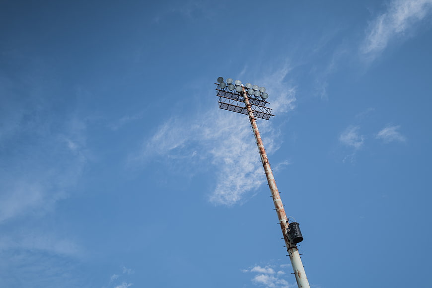 Rusty stadium floodlight pole against blue sky