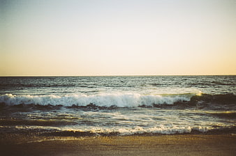 Serene Ocean Waves Rolling onto Sandy Beach at Sunset