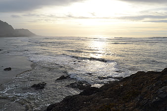 Sunset over rocky coastline with gentle waves and misty hills